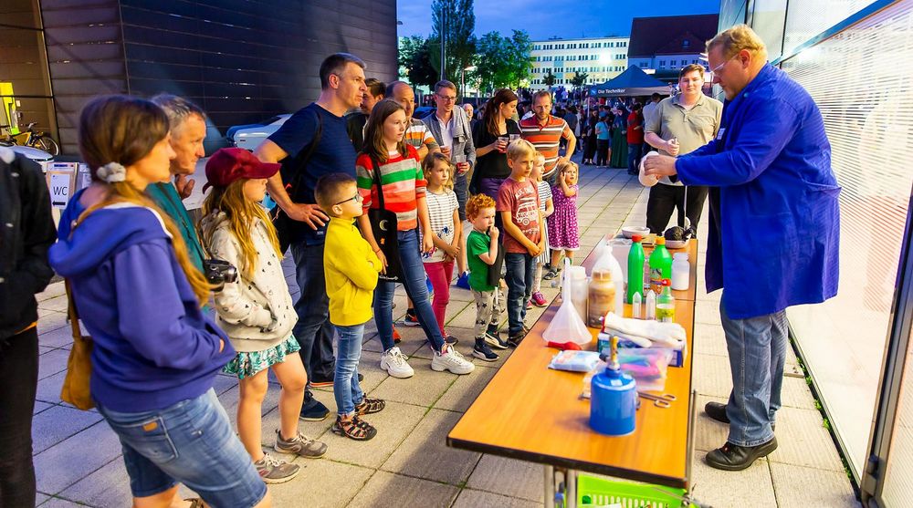 Foto: Ein Mann experimentiert im Abendlicht vor Besuchern der Langen Nacht der Technik.