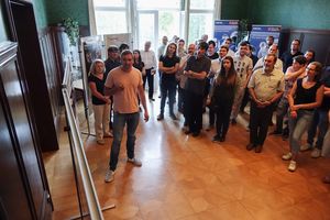 Foto: Gruppenbild. Teilnehmer betrachten stehend eine Posterpräsentation.