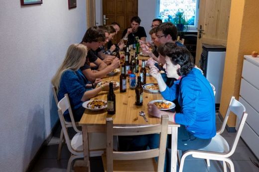 Foto: 11 Studierende sitzen an einem langen Tisch beim gemeinsamen essen.