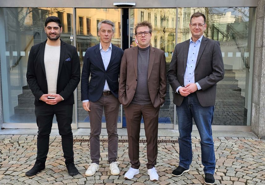 Gruppenbild mit vier Personen vor einer Glastür. 