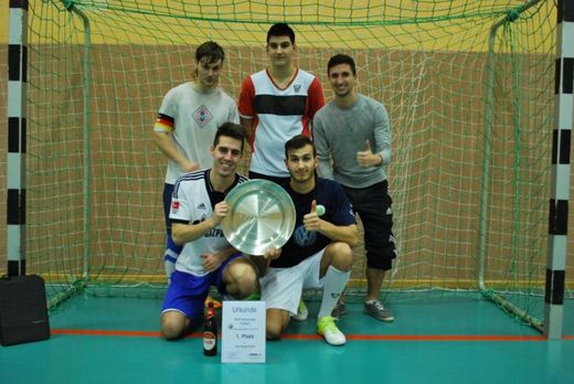 Foto: Gruppenbild. 5 Männer einer Sportgruppe stehen mit Siegerschale und Urkunde in einem Handballtor.