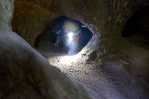 Foto: Outdoor. Eine Person mit Helmlampe kriecht durch niedrige Höhlengänge.