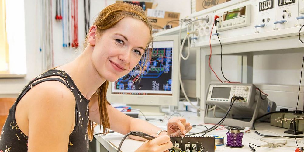 Foto: Eine Studierende sitzt an einem Laborarbeitsplatz und lötet an einer Leiterplatte.