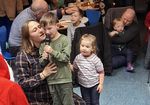 Ein Kind spricht in ein Mikrophon und sagt ein Gedicht an. Mutter und kleine Schwester sitzen daneben.