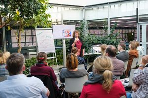 Foto: Person hält vor sitzendem Publikum Vortrag