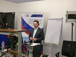 Foto: Ein Mann steht vor einem Plakat und einem Flipchart, im Vordergrund stehen viele technische Geräte.
