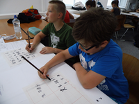 Foto: Zwei Schüler sitzen in einem Lehrraum der Fakultät Sprachen und zeichnen auf ein Papier chinesische Schriftzeichen von der Tafel ab.
