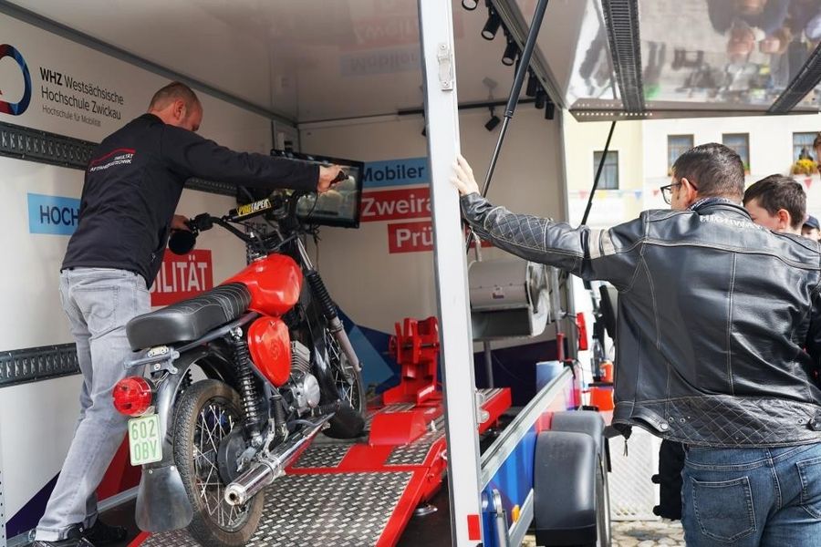 Eine Person schiebt einen Simson-Roller auf den Prüfstand. 