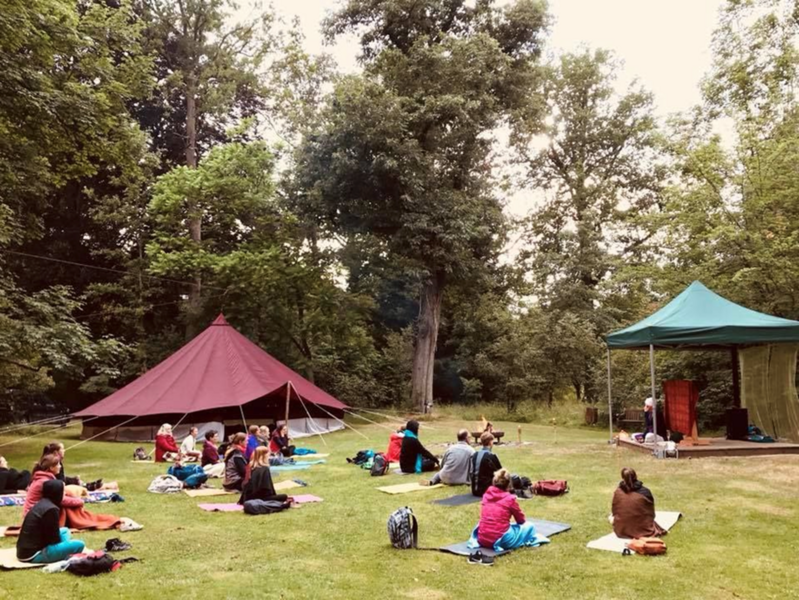 Personen sitzen auf Wiese vor einer Jurte