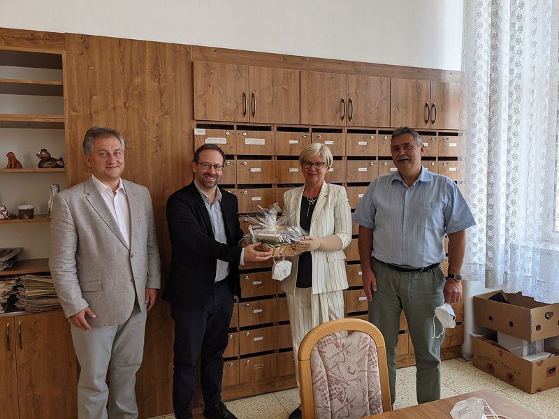 Foto: Drei Männer und eine Frau stehen vor einem Schrank. Einer der Männer und die Frau halten ein Geschenk.
