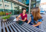 Foto: Zwei Studierende sitzen im Freien vor der Hochschulbibliothekt und schauen auf ein Tablet.