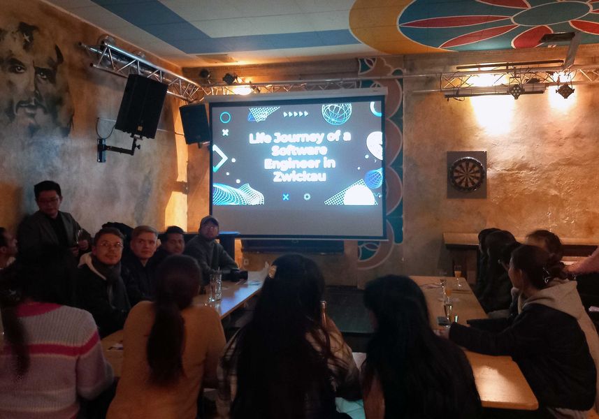 Gruppe von internationalen Studierenden sitzt im Studentenclub Tivoli und schaut auf eine Leinwand. 