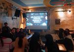 Gruppe von internationalen Studierenden sitzt im Studentenclub Tivoli und schaut auf eine Leinwand.
