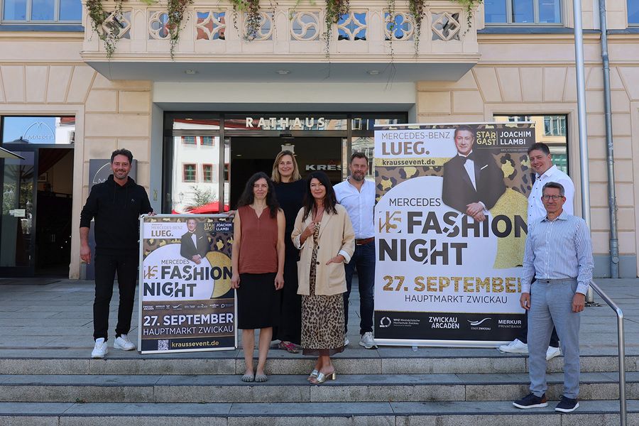 Eine Gruppe von Personen steht vor dem Rathaus und präsentiert Veranstaltungsplakate zur Fashion Night. 