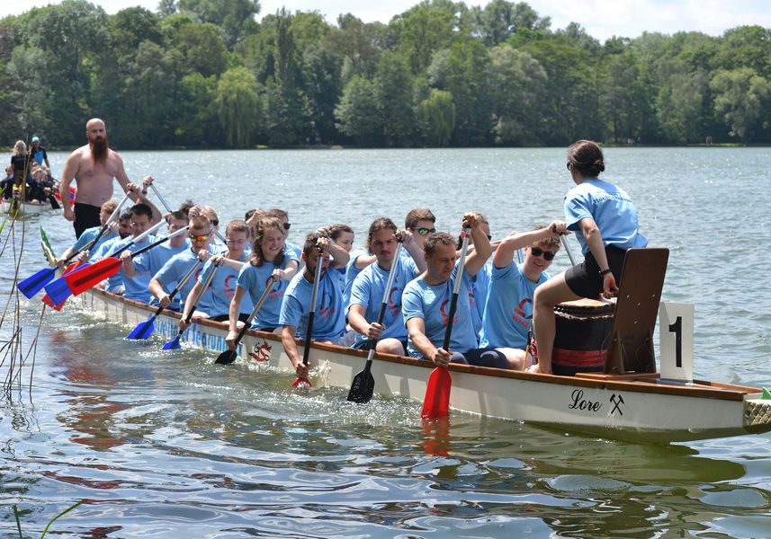 Team aus Männern und Frauen in hellen T-Shirts auf einem Teich im Drachenboot