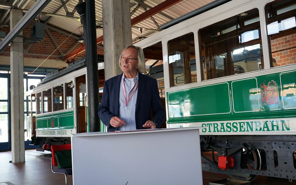 Dr. Peter Mietke steht an einem Rednerpult, im Hintergrund ist eine historische STraßenbahn zu sehen. 