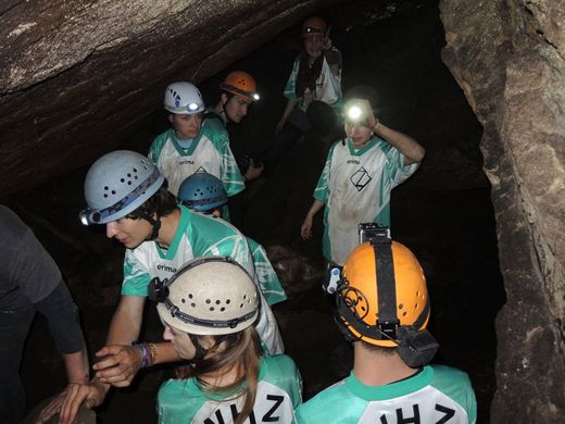 Foto: Outdoor. Teilnehmer mit Helmlampen erkunden eine Höhle.