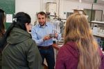 Mann hält Forschungsinstrument in der Hand und zeigt dieses drei Besucherinnen