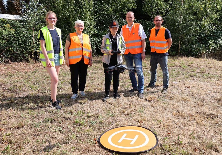 fünf Personen in Warnwesten stehen auf einer Wiese und steuern eine Drohne