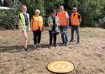 fünf Personen in Warnwesten stehen auf einer Wiese und steuern eine Drohne