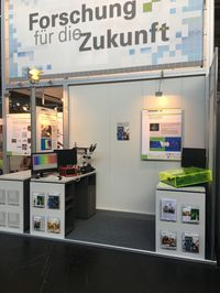 Foto: Ein kleiner Messestand. Aufschrift: Forschung für die Zukunft.