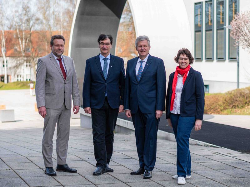 Vier Personen stehen auf dem Campus nebeneinander.