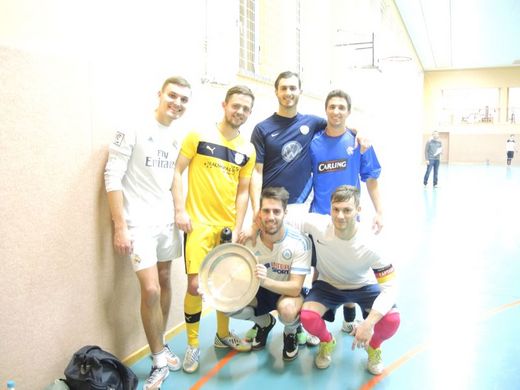 Foto: Gruppenbild einer 6 Personen Mannschaft mit einer Siegerschale in einer Sporthalle.