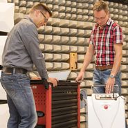 Foto: Zwei Mitarbeiter im EMV Labor arbeiten an technischen Geräten.