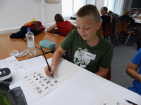 Foto: Ein Schüler sitzt in einem Lehrraum der Fakultät Sprachen und zeichnet auf Papier chinesische Schriftzeichen von einer Vorlage ab.