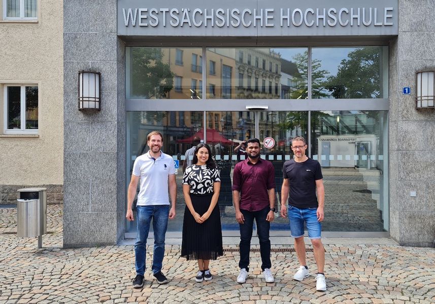 vier junge Forscher, davon eine Frau, stehen vor einer Hochschule und schauen in die Kamera