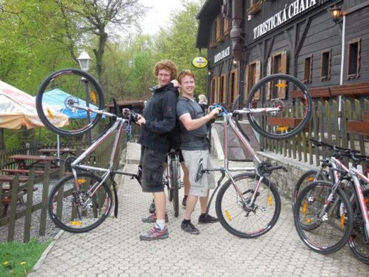 Foto: Zwei Mountainbiker halten ihre Räder auf dem Hinterrad stehend hoch und lächeln in die Kamera.