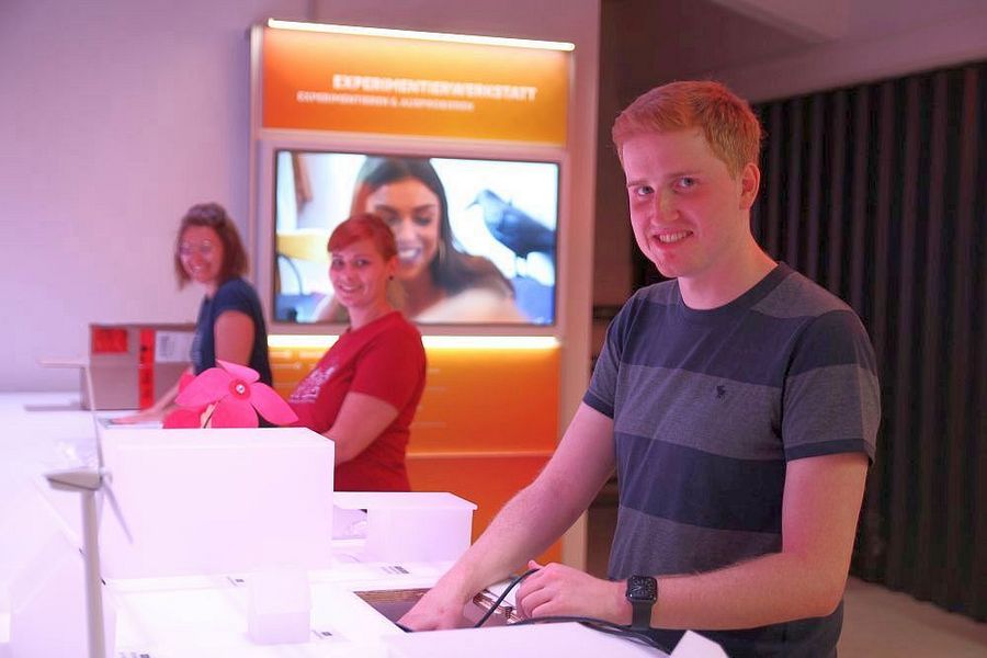 Foto: Drei Studierende stehen an Ausstellungsstücken zum Thema "Wissenschaft zum anfassen" und lächeln in die Kamera.