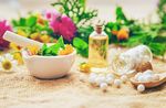Foto: Utensilien für Naturheilverfahren mit Mörser, Stößel, kleinen Flaschen und runden Kügelchen verteilt auf einem Tisch.