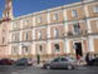 Foto: Eine Gebäudefassade der Universidad de Huelva mit davor parkenden Autos am Straßenrand.