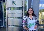 junge Frau mit langen, dunklen Haaren hält glücklich ihr Abschlusszeugnis in die Kamera