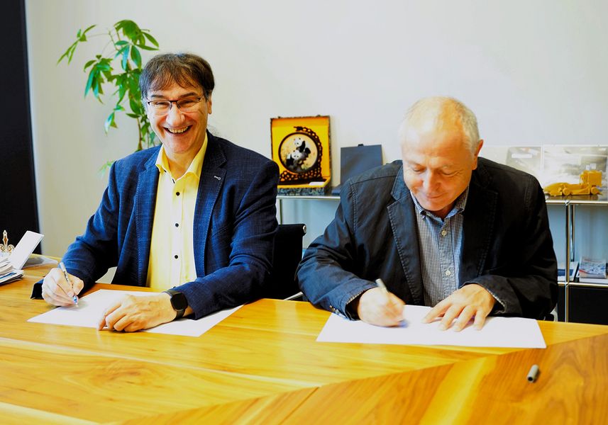 zwei Herren sitzen an einem Schreibtisch und unterzeichnen einen Vertrag