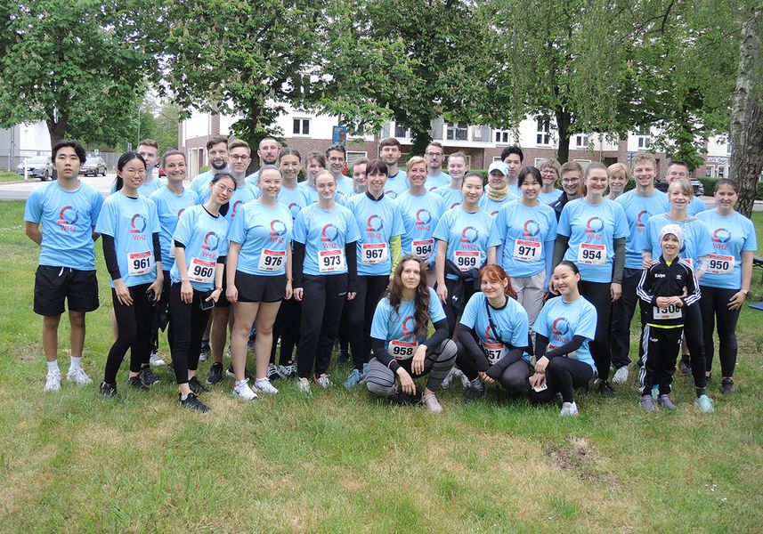 Gruppe von jungen Frauen und Männern in hellblauen Sportshirts auf einer grünen Wiese