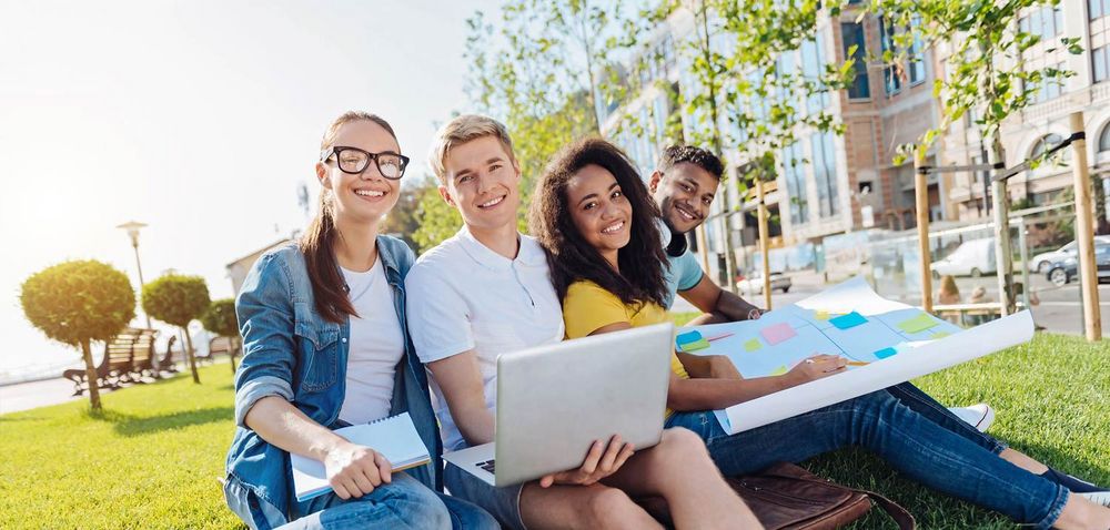 Vier Studierende sitzen draußen zusammen und lächeln in die Kamera. Quelle: zinkevych/fotolia