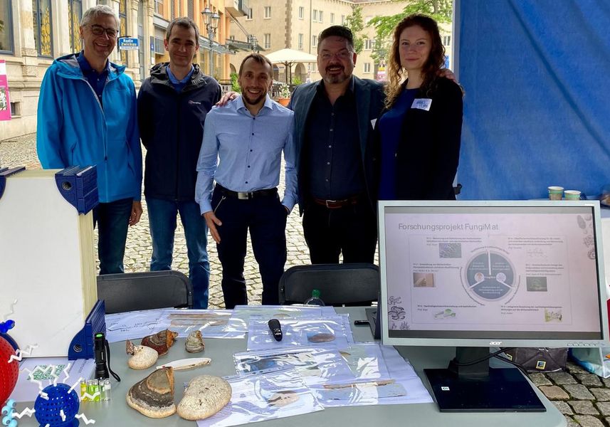 Gruppen von fünf jungen Menschen eng zusammenstehend an einem Stand auf einem Markt