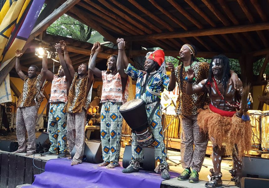 Musikgruppe mit folkloristischer Kleidung und Kostümen winkt ins Publikum. 