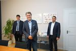 Foto: Drei Männer stehen versetzt in einem Büro und lächeln in die Kamera.