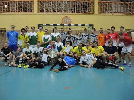 Foto: Gruppenbild mehrerer Mannschaften vor einem Handballtor in einer Sporthalle.