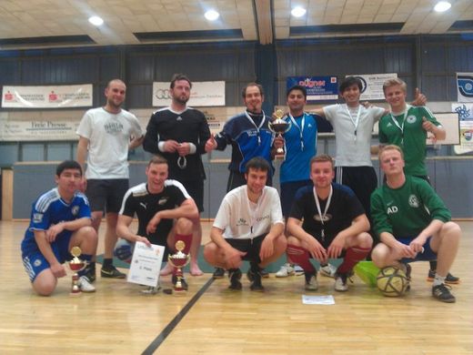 Foto: Gruppenbild. 11 Männer einer Sportgruppe stehen mit Siegerpokalen und Urkunde in einer Sporthalle.