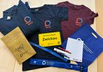 T-Shirts, Jacken, Frühstückbrettchen und weitere Werbeartikel mit dem logo der Westsächsischen Hochschule Zwickau liegen auf einem Tisch.