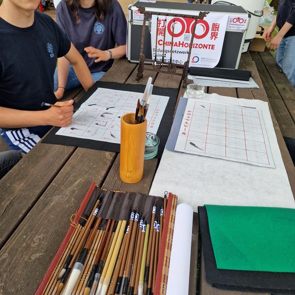 Auf einem Tisch liegen Kalligraphie-Stifte, Pinsel und Papier. 
