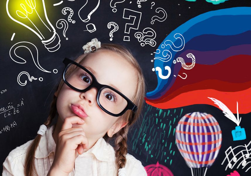 Mädchen mit langen Haaren und Brille im Grundschulalter steht vor einer Tafel und überlegtTafel und hat 