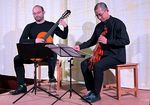 zwei Männer in schwarzer Bekleidung sitzen auf einer Bühne und spielen Gitarre und Violine