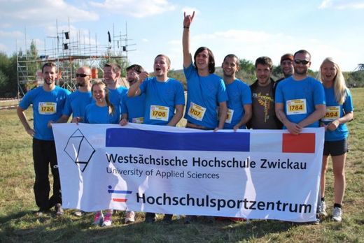 Foto: Gruppenbild. Teilnehmer einer Sportgruppe stehen zusammen und halten das Banner des Hochschulsportzentrum vor sich.