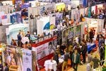 Blick von oben in eine Messehalle. Aussteller und Besucher unterhalten sich an den verschiedenen Ständen.