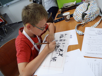 Foto: Ein Schüler sitzt in einem Lehrraum der Fakultät Sprachen und zeichnet auf ein Papier chinesische Schriftzeichen von einer Vorlage ab.